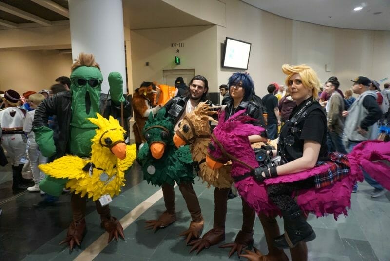 Four cosplayers dressed as characters from Final Fantasy XV. They are riding hand-made chocobos.