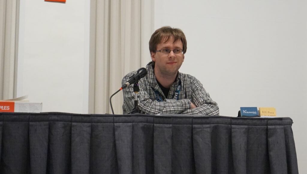 Anime Boston 2019 - Foundations of World Building - BH Pierce Sits at a table as he presents a lecture.