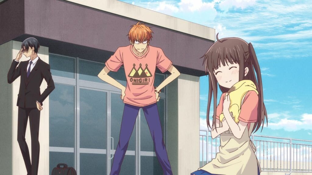 Fruits Basket (2019) Anime Still - Tohru Honda holds a yellow rabbit (Momiji Soma), as Kyo looks on angrily. Hatori facepalms in the background.