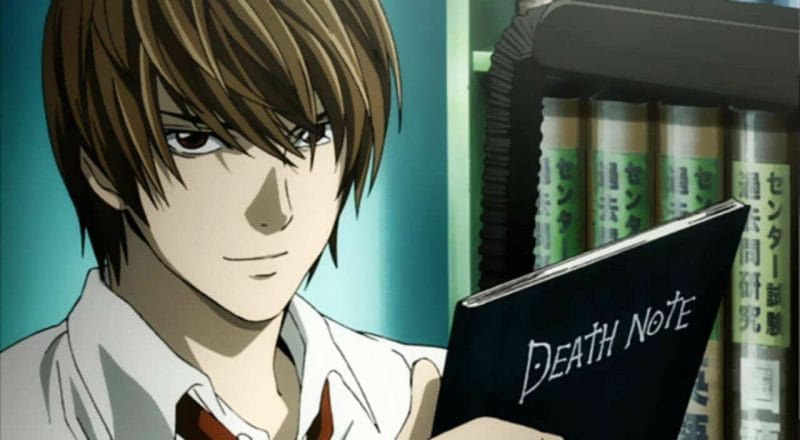 Death Note still - Light Yagami poses with the titular Death Note.