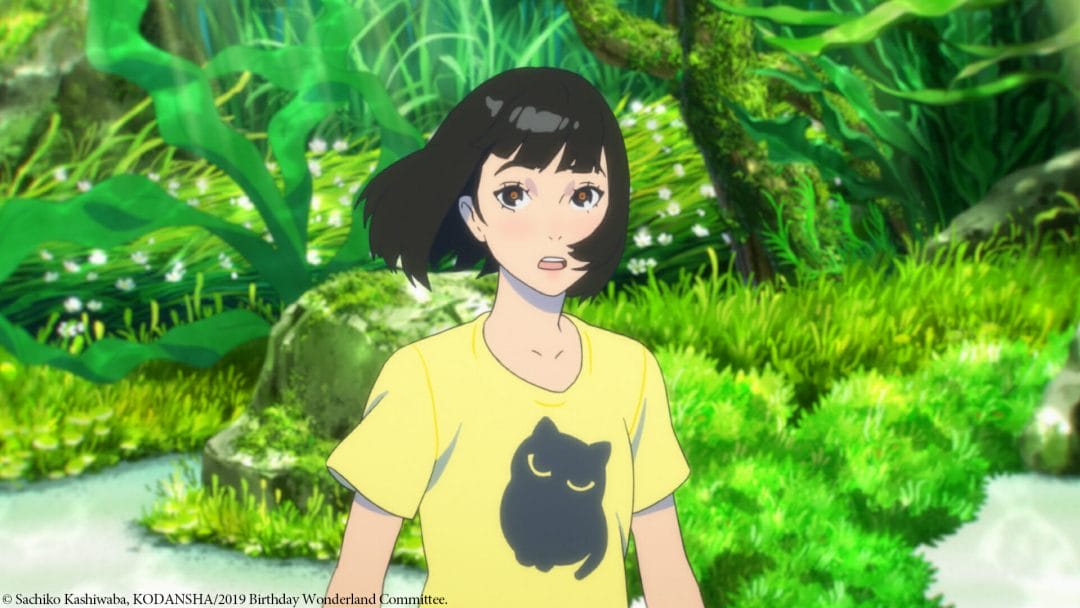 A woman with black hair, wearing a yellow T-shirt stands in a forest. The wind is blowing, causing her hair to be swept to the side.