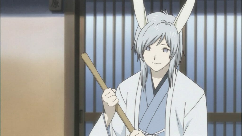 Natsume's Book of Friends Anime Still - A man with silver hair and rabbit ears smiles as he holds a broom