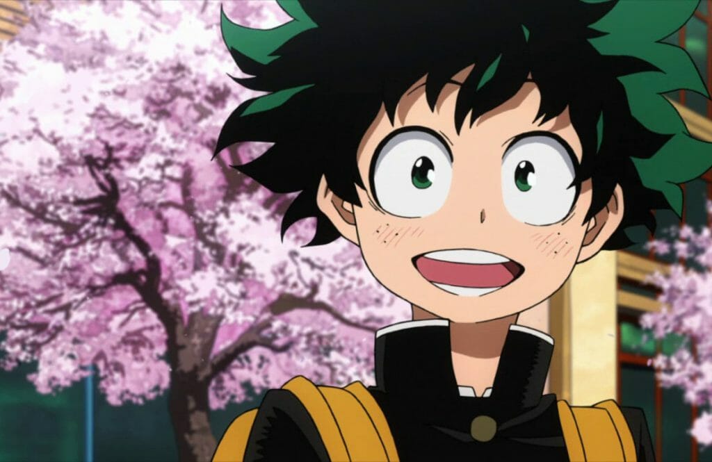 My Hero Academia anime still - a boy with shaggy green hair smiles in front of blooming cherry blossom trees.
