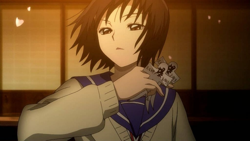 A dark-haired woman wearing a school uniform holds a mystical charm.