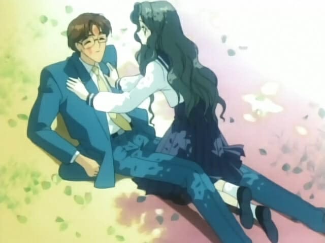 A dark-haired woman lays atop a brown-haired man in a suit.
