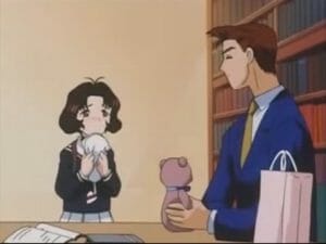 A young girl looks expectantly at a brown-haired man holding a teddy bear.