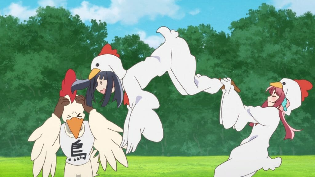 A black-haired woman in a chicken costume jumps at a gigantic chicken mascot. A red-haired woman, also in a chicken costume, holds the other woman back.