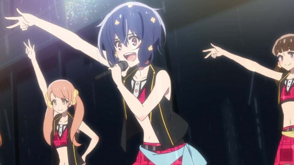 Still from Zombie Land Saga Episode 6, which depicts a black-haired idol smiling brightly as she addresses a crowd from the stage.