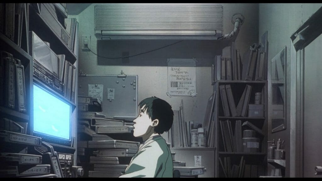 Still from Patlabor 2, which features a black-haired man sitting in a cluttered office as he stares at a glowing blue screen.