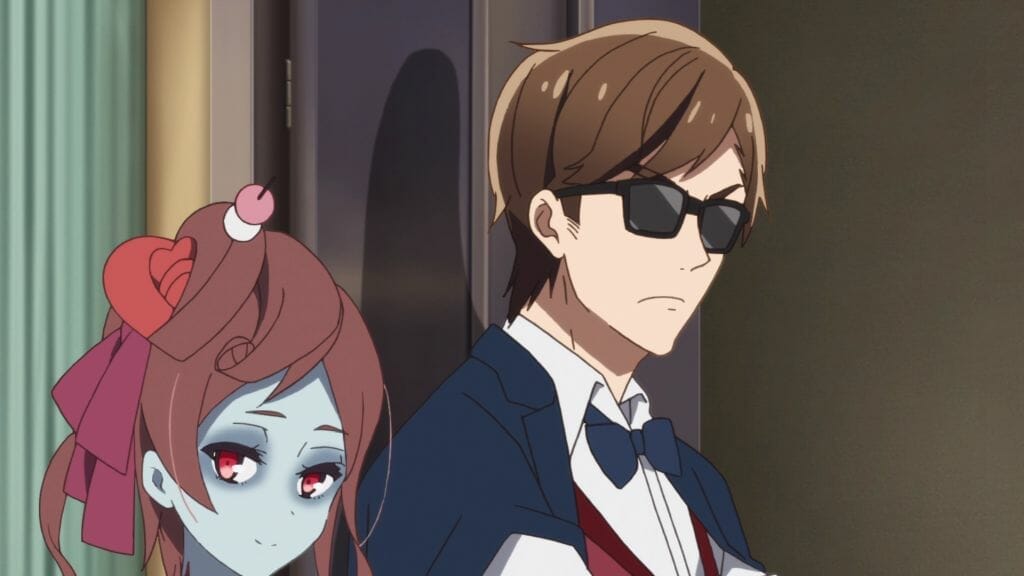 Still from Zombie Land Saga Episode 10, which features a brown-haired zombie woman standing beside a man in sunglasses. Both are wearing worried expressions
