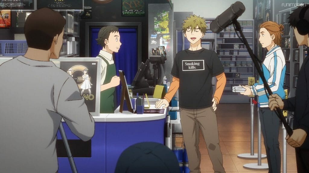 Ikebukuro West Gate Park Episode 6 that depicts two men at a counter in a video store. The man on the right smiles smugly as the man on the left stares. The two are surrounded by a camera crew.