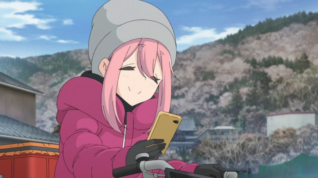 Still from Laid Back Camp that features Nadeshiko smiling as she looks down at her smartphone.