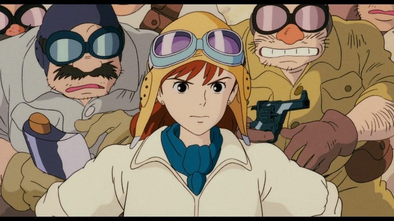 Still from Porco Rosso that focuses on a woman in a flight suit and aviator cap. She's standing, defiant, as several men look on nervously behind her.