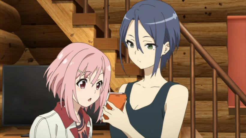 Still from Sakura Quest - A black-haired woman in a tank top shows her cell phone to a pink-haired woman.