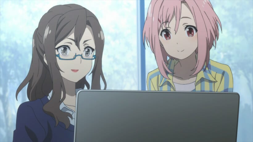 Still from Sakura Quest - A pink-haired woman an da brown-haired woman in glasses look at a computer monitor.