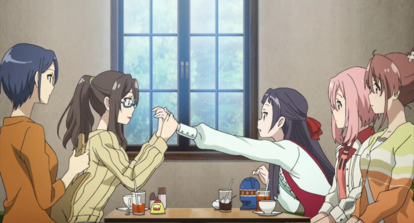 Still from Sakura Quest - Five women are gathered aroun da table. A brown-haired woman with glasses is holding the hands of a black-haired woman, who appears shocked.