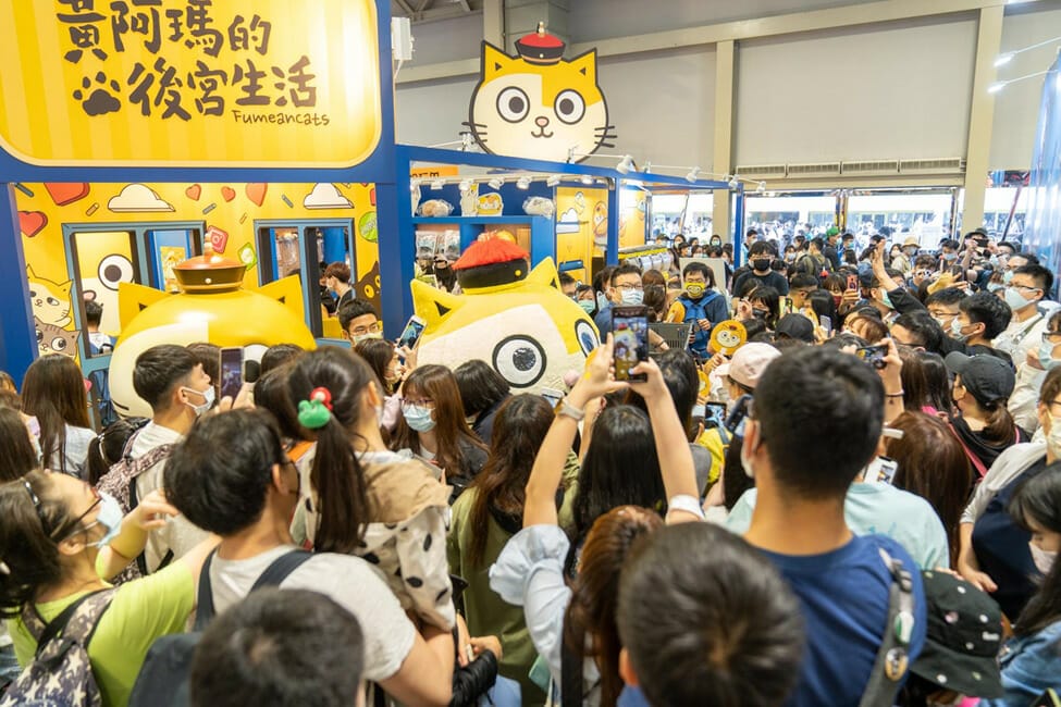 A mascot character of a yellow-and-white cat wearing a red hat stands amid a crowd of people