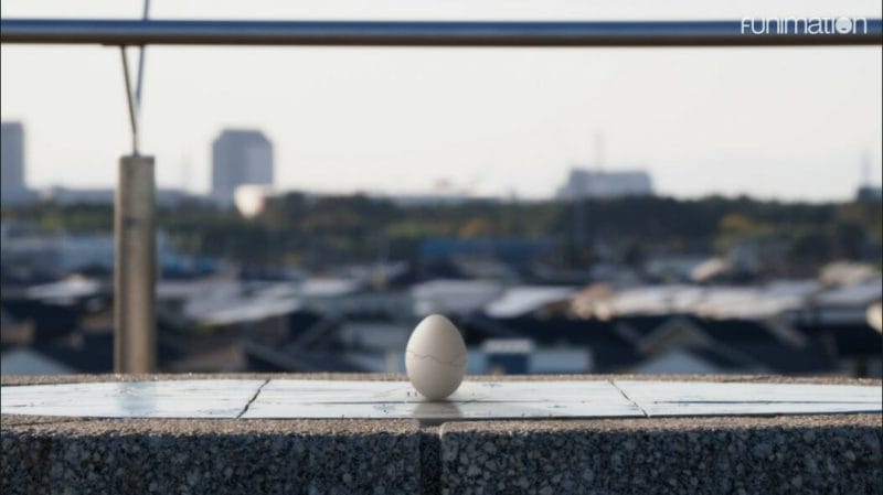 A single, white egg with a hairline crack in it, sitting in front of a city skyline