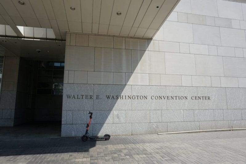 A scooter is propped against a grey brick wall with the word "Walter E. Washington Convention Center" posted on it.
