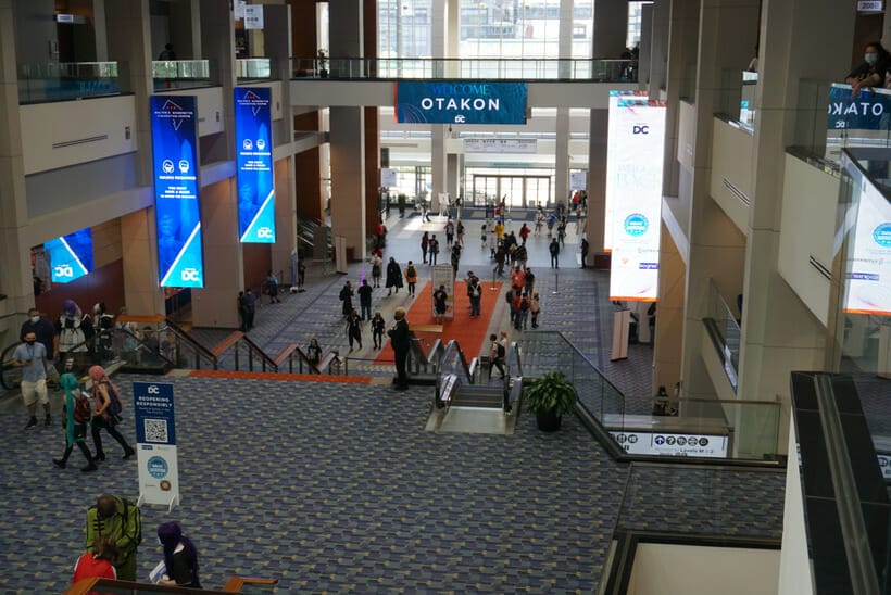 Photograph of the Walter E. Washington Convention Center's main floor. Several attendees mill about beneath a sign that says "Welcome to Otakon 2021"