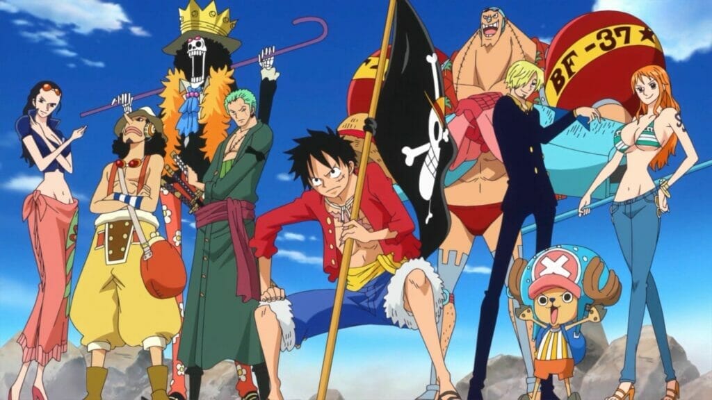 The crew from One Piece stands on a rock formation, before a clear blue sky.