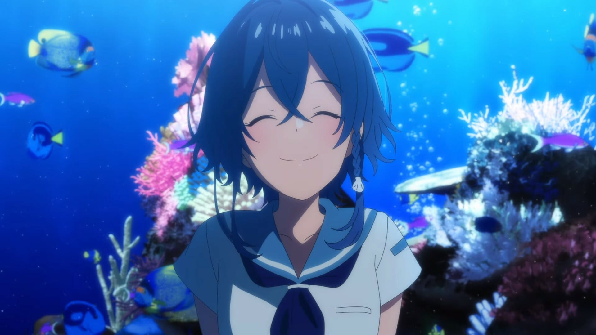 A blue-haired girl in a school uniform smiles as she stands in front of an aquarium.