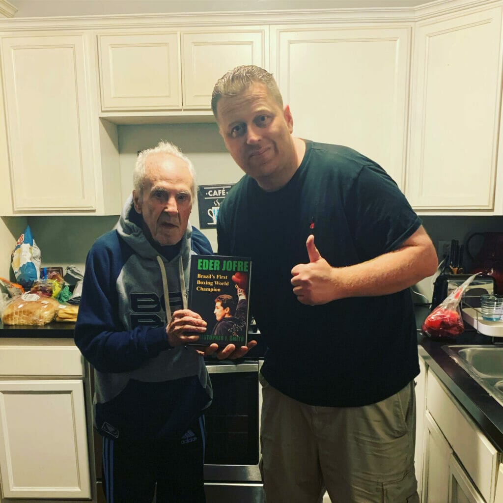Photograph of Eder Jofre and biographer Christopher J. Smith; Jofre is holding a copy of "Eder Jofre: Brazil's First Boxing World Champion"