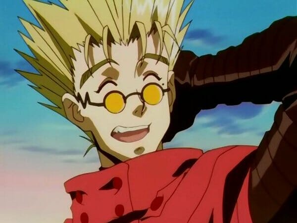 Image of Vash the Stampede - a lanky, blonde man wearing sunglasses and a red coat, as he smiles awkwardly.