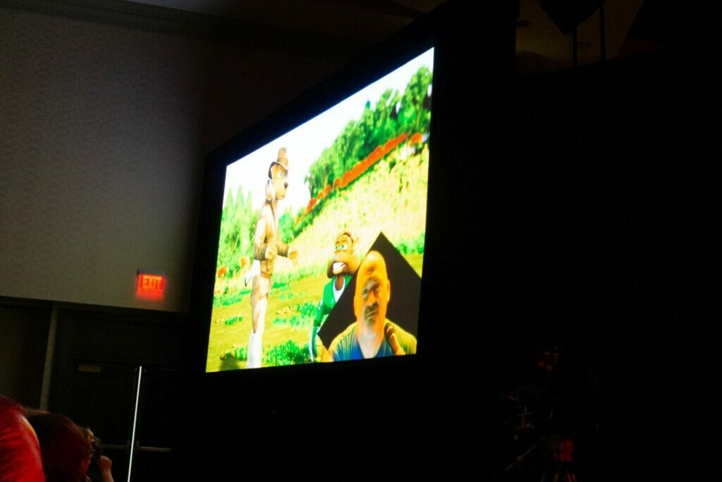 Photo of a screen depicting a cartoon dog and squirrel holding a conversation. In the bottom right corner of the image is a video feed of a man with a perplexed expression.