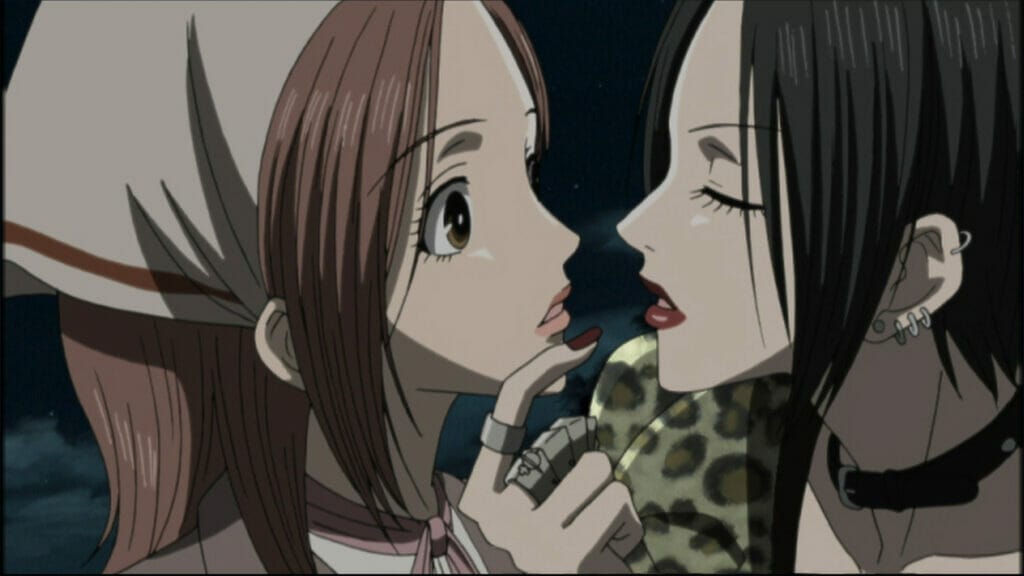 Still from the Nana anime, which depicts a brown-haired woman wearing a headscarf who looks unsure as a black-haired woman moves in to kiss her.