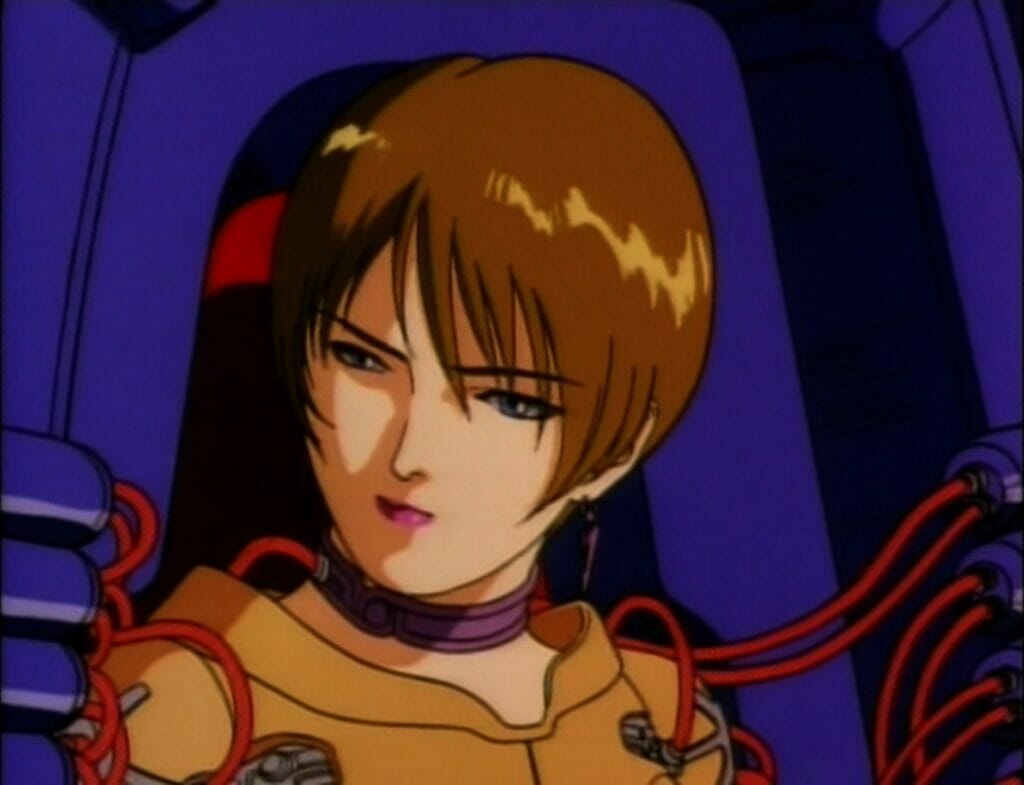 Screenshot from Genocyber. A woman with short brown hair cut in a bob cut looks away, disdainfully. She is hooked up to a machine with red wires extending from it.
