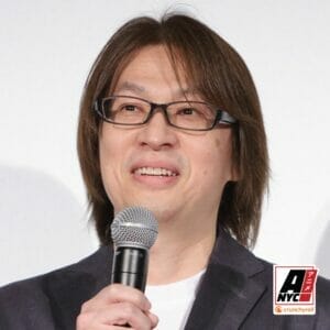 Head shot of Shuko Murase, a Japanese man with medium-length brown hair and glasses, as he holds a microphone.