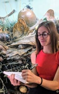 Photo of cartoonist Sofia Warren, who is wearing glasses and a red top as she holds a sketchbook.