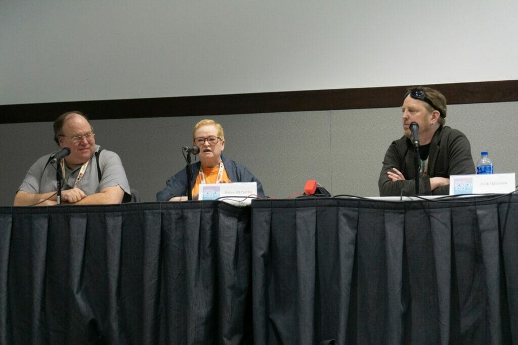 Photo of a balding, bespectacled man in a grey polo shirt, a woman with short, light hair wearing glasses and a grey overshirt, and a brown-haired bearded man in a grey suit jacket and T-shirt. The man in the jacket has a pair of goggles resting at his hairline.