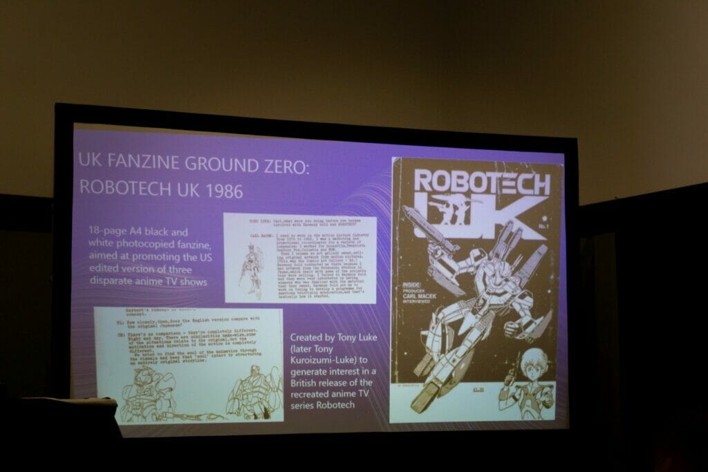 Photo of a PowerPoint slide depicting a copy of Robotech UK Magazine. Text: UK Fanzine Ground Zero: Robotech UK 1986 18-page A4 black and white photocopied fanzine, aimed at promoting the US edited version of three disparate anime TV shows. Created by Tony Luke (alter Tony Kuroizumi-Luke) to generate interest in a British release of the recreated anime TV series Robotech.
