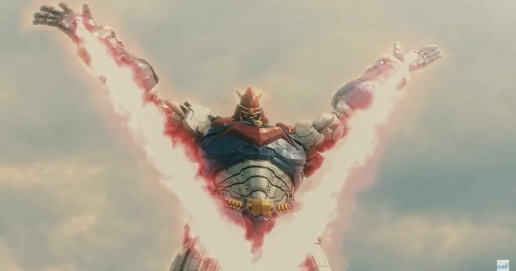 Photo of Voltes V, a red, yellow, blue, and silver robot. Its arms are spread wide, as a giant flaming "V" forms between them.