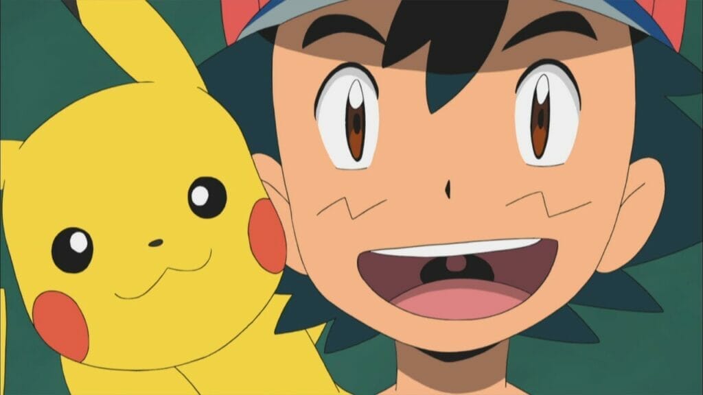 Ash Ketchum - a boy with shaggy black hair and a red baseball cap - smiles as he looks toward the camera. Pikachu is perched on his shoulder.