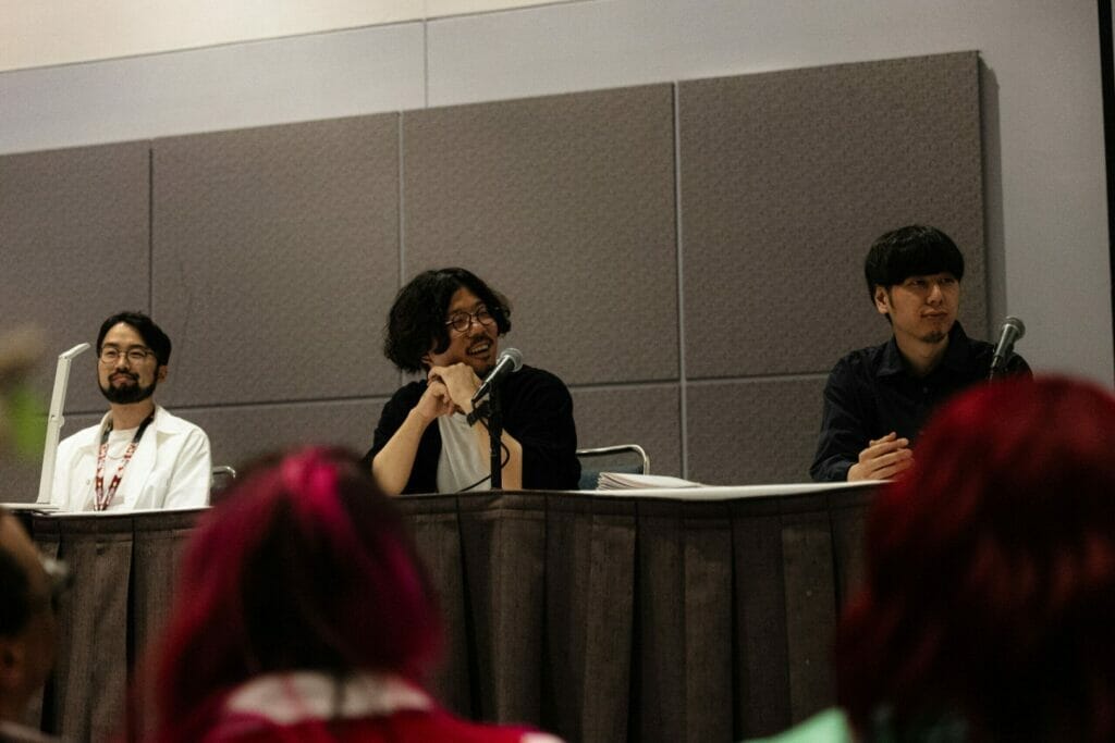 Three members of the Ancient Magus' Bride anime staff sit at a table as they talk amongst each other.