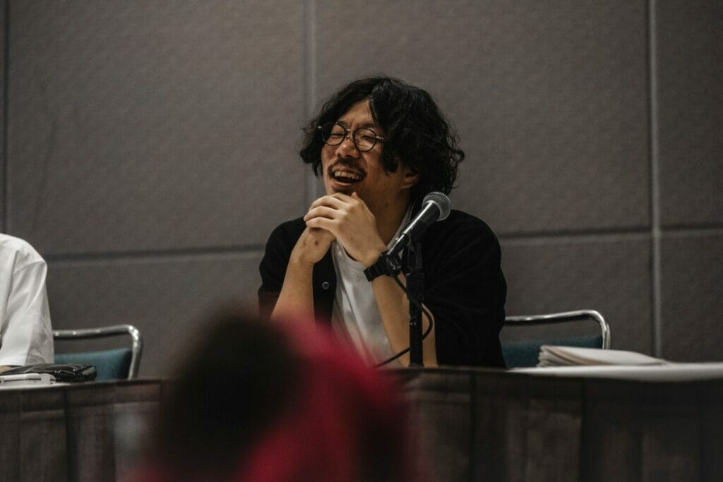 A member of the Ancient Magus' Bride anime staff delivers a thoughtful expression as he speaks to an audience.