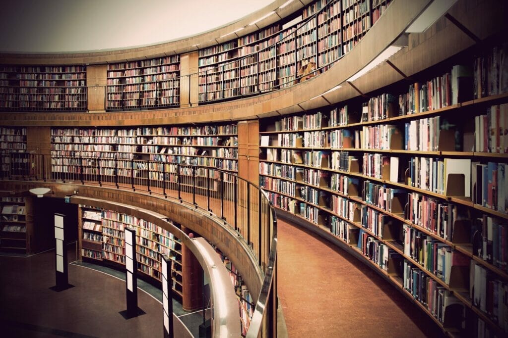 Photograph of a round room in a public library, with three shelves of books that extend to the ceiling. Photographer: PinkBadger, used under license.