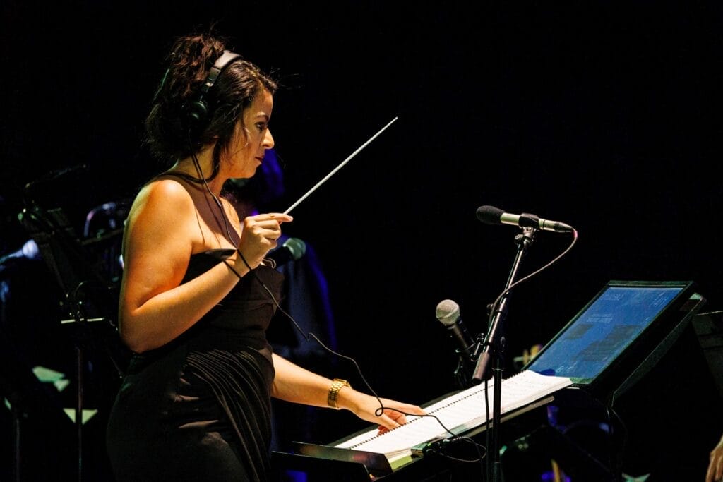 Photograph of conductor Macy Schmidt, who is wearing a black dress and holding a conductor's baton as she reviews a score in front of her