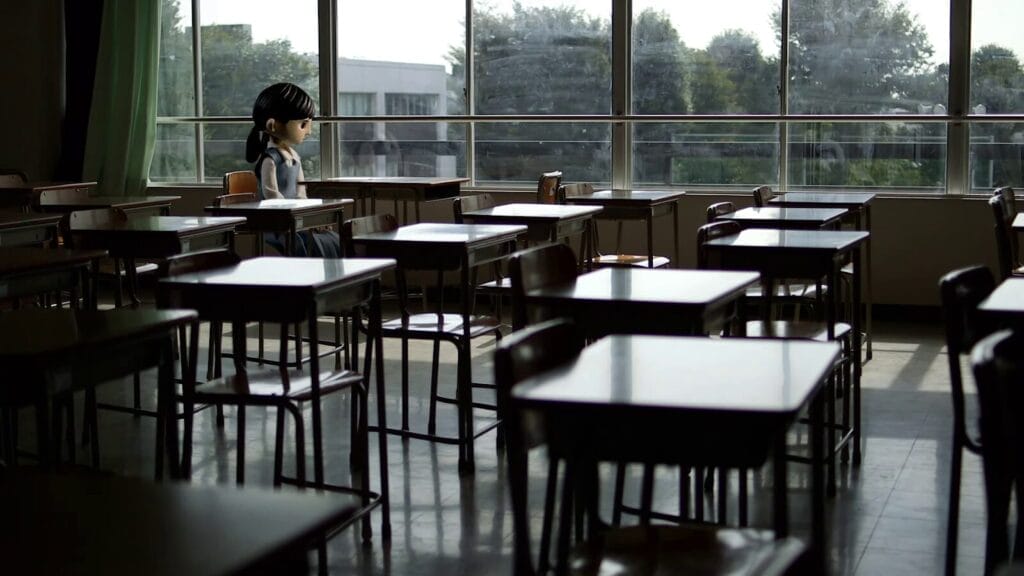 Screenshot from The Question that depicts a girl sitting alone at a desk, in an empty classroom.