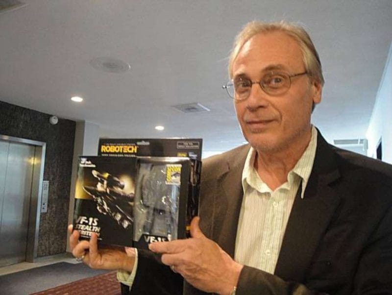 Carl Macek poses in a promotional photo, while holding a Robotech action figure.