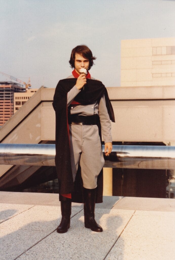 Photograph of Robert Fenelon dressed as Desslock from Star Blazers. He's holding a white flower on the roof of the Baltimore Convention Center at Worldcon 1983