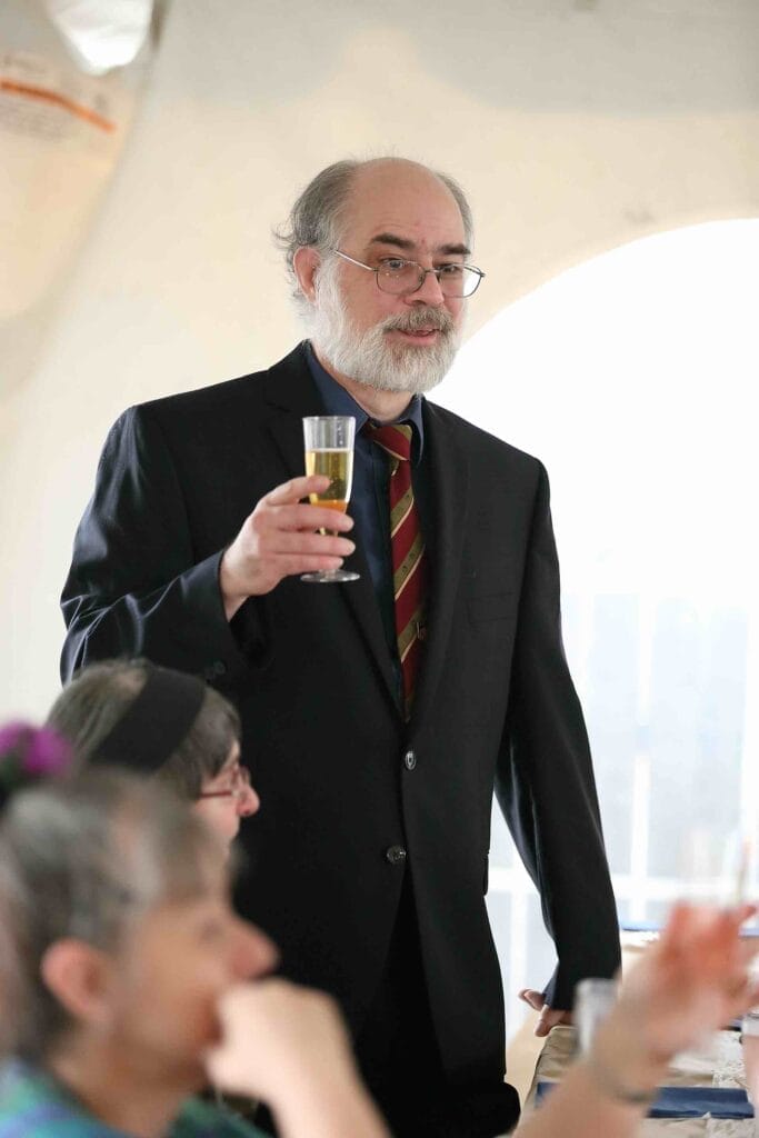 A photo of Robert Fenelon taken in 2016. He's an older gentleman with a beard, wearing a dark suit.