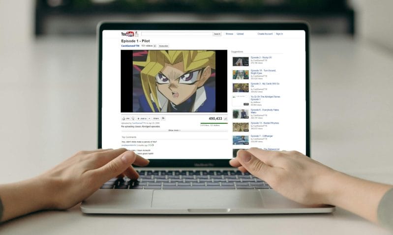 A photo of a person using a laptop, which features a classic YouTube interface on the screen. The featured video is "Yu-Gi-Oh! Abridged" episode 1