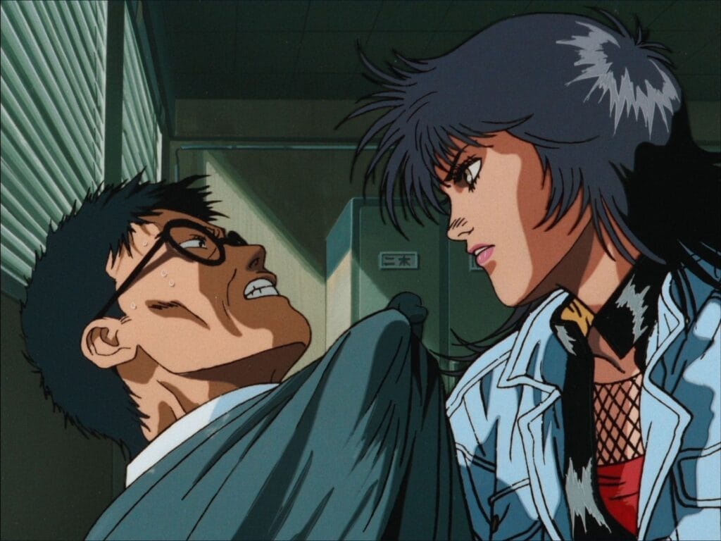 Screenshot from Angel Cop that depicts Angel, a black-haired woman in a jean jacket and red top, threatening a bespectacled man in a suit.