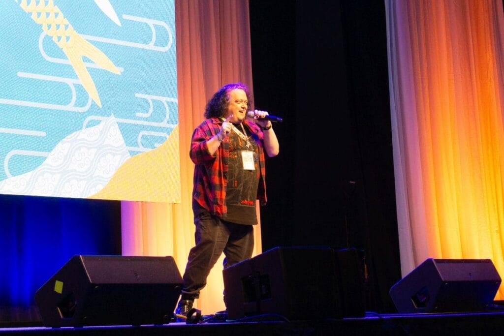 Voice actor Greg Ayres stands onstage at Anime Boston 2024's opening ceremonies