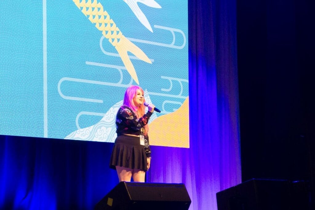 Voice actor Kira Buckland stands onstage at Anime Boston 2024's opening ceremonies
