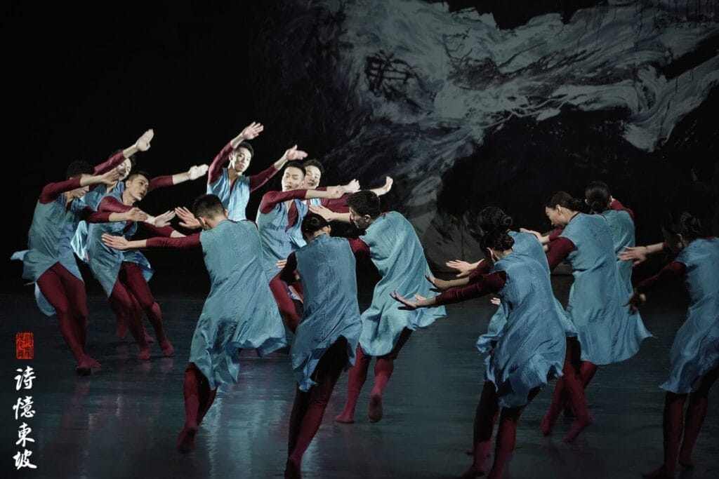 Photograph from Dongpo: Life In Poems that depicts dancers wearing blue and red on a stage, against a black-and-white background.